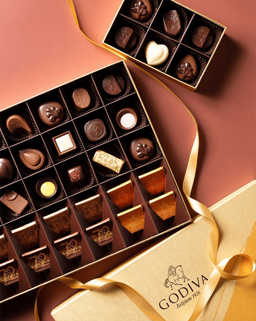 A box of Godiva chocolates with ribbon and chocolate-dipped treats
