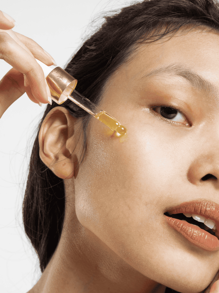 A woman applying skincare serum from a glass dropper